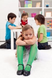 full size featured image of a girl is left out where three other kids in the background are playing without her.