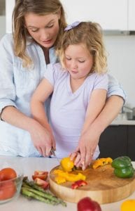 Child learning to chop vegetables, capsicum, from mother