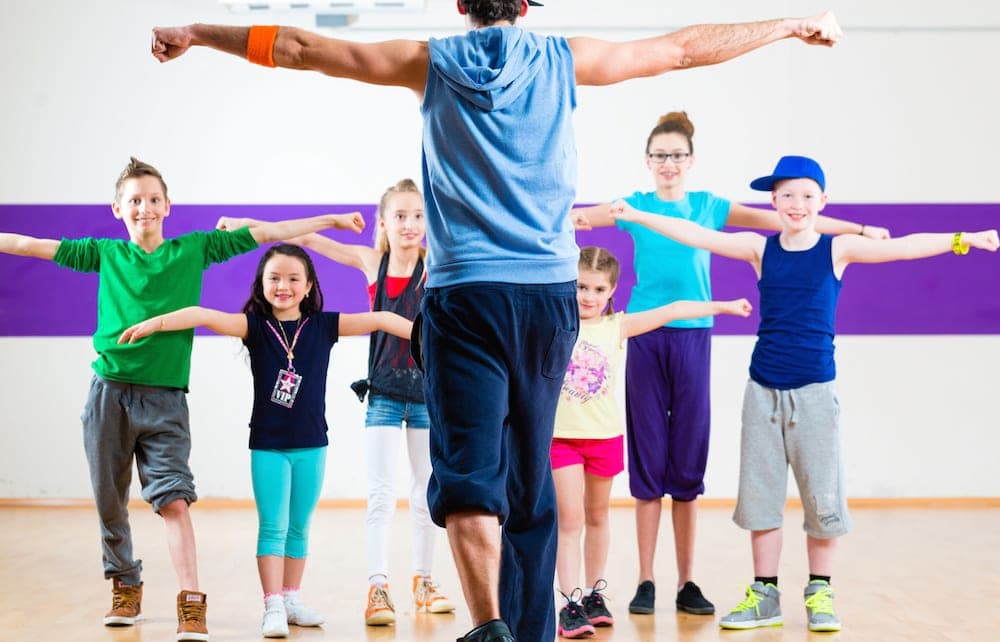 Dance Classes Gold Coast - Dance teacher giving children Zumba fitness class in gym
