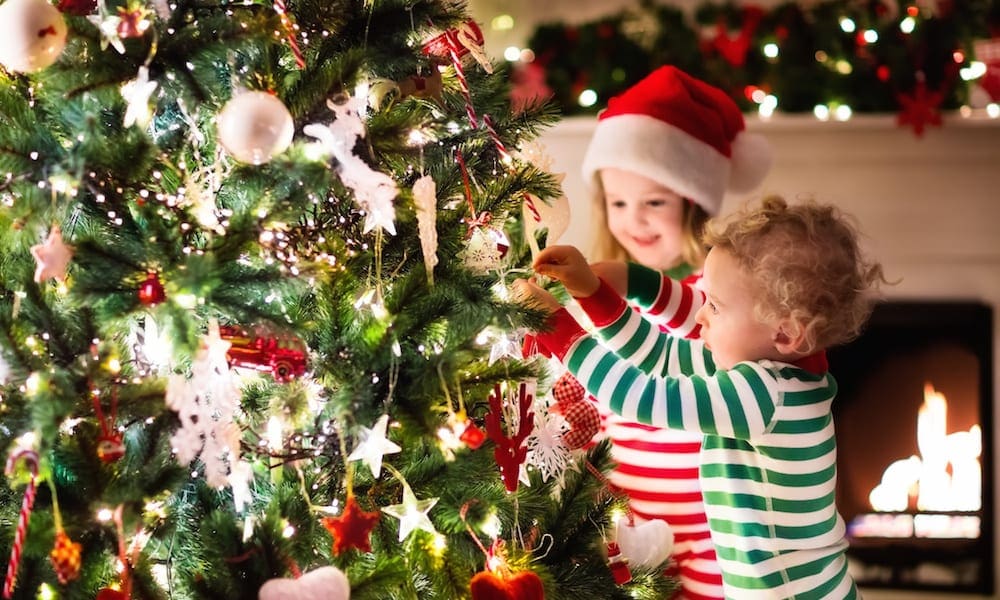 Where to buy a real christmas tree gold coast Happy little kids in matching red and green striped pajamas decorate Christmas tree in beautiful living room with traditional fire place. Children opening presents on Xmas eve.
