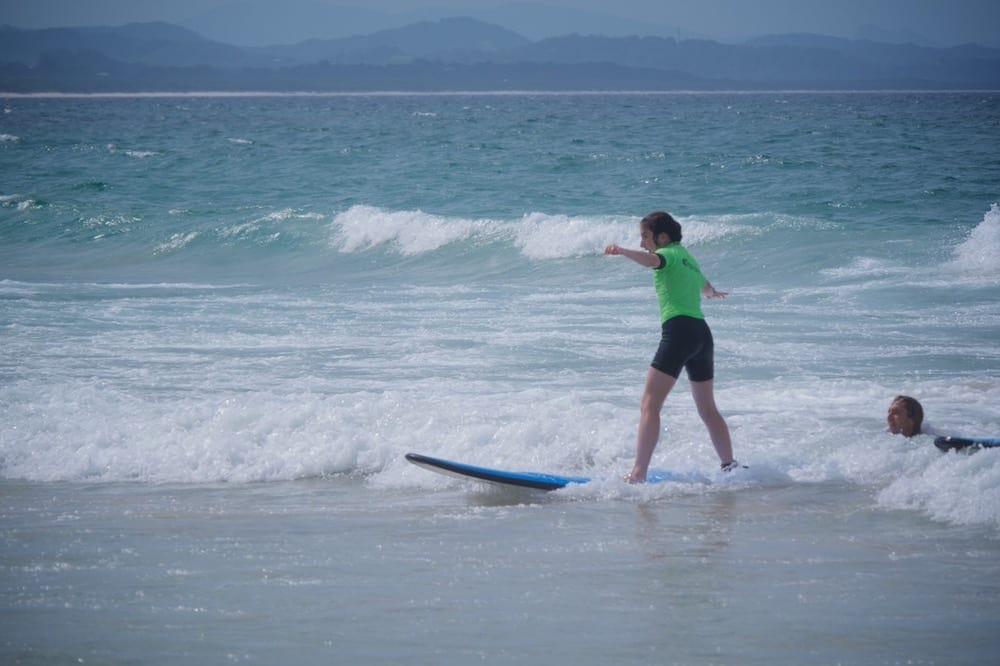 Family Surfing Lessons Young girl catches wave into shore on sunny day