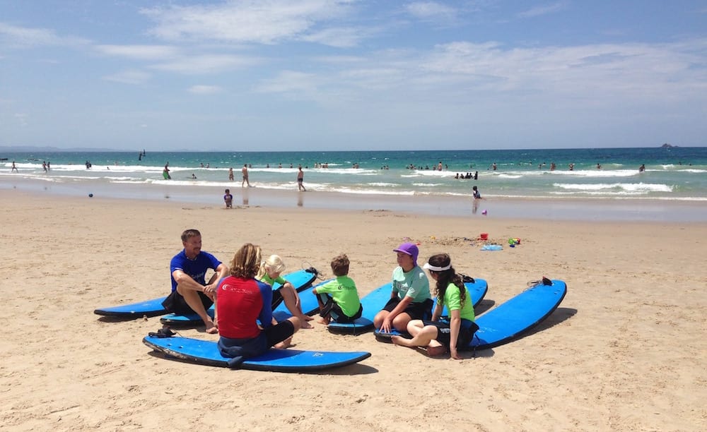Family Surfing Lessons family sitting on beach with surf instructor