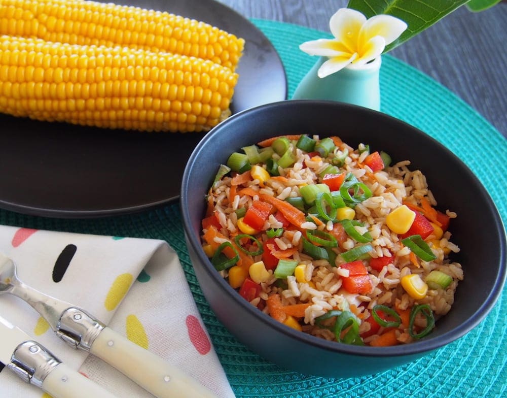 best rice salad black bowl with rice salad next to black plate with two corn kernels, and by a vase featuring one frangipani flower and leaf