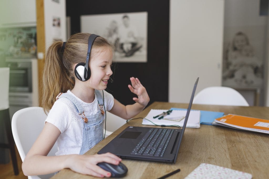 Child studying at home waving to her online tutor