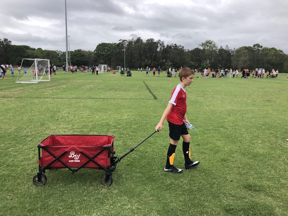 Boy dragging red Buddy Wagon at soccer match