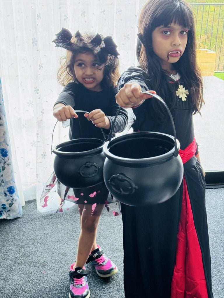 Two children in Halloween costumes holding black cauldrons, ready to go trick-or-treating.