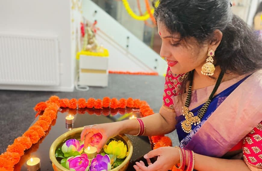 Woman decorating her home for Deepavali, lighting a diya in a brass bowl with colourful lotus candles and marigold flowers during the Festival of Lights celebration.