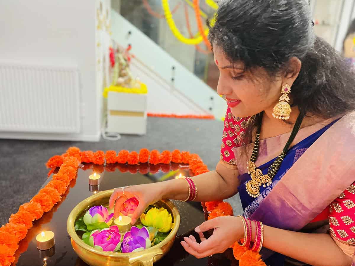 Woman decorating her home for Deepavali, lighting a diya in a brass bowl with colourful lotus candles and marigold flowers during the Festival of Lights celebration.