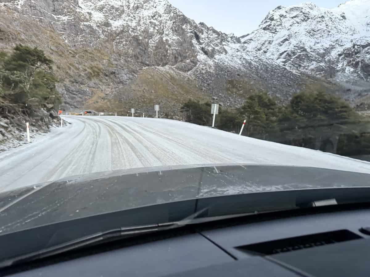 Snow-covered mountain road on the scenic drive towards Milford Sound, viewed from inside the car on a winter morning in New Zealand