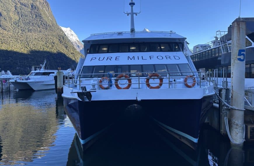 Pure Milford cruise boat docked at Milford Sound with mountains reflecting in the calm water