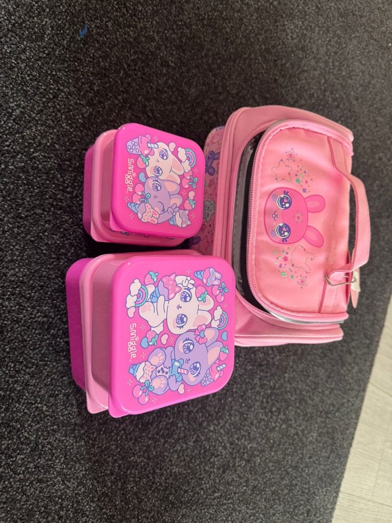 Smiggle lunch box set placed next to the matching pink lunch bag with cute character print.