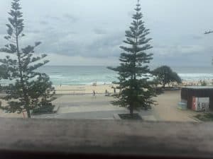 Beachfront view of Surfers Paradise on the Gold Coast, with pine trees, waves, and people enjoying the foreshore.