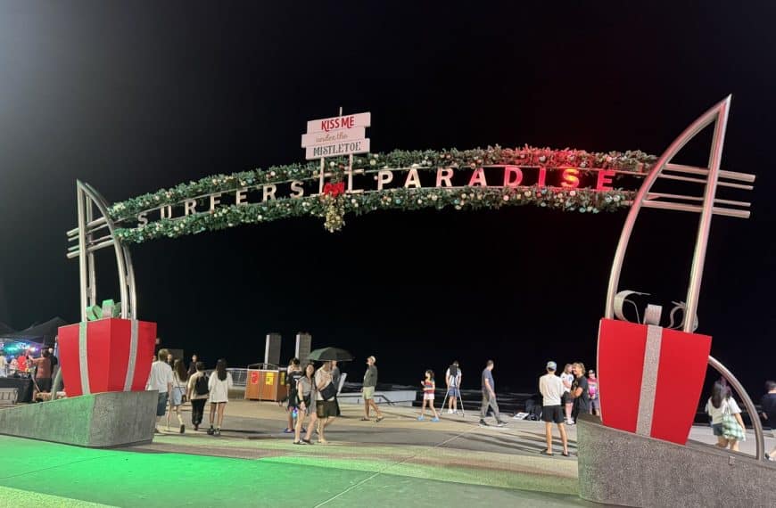 Surfers Paradise sign lit up at night with families walking along the Esplanade